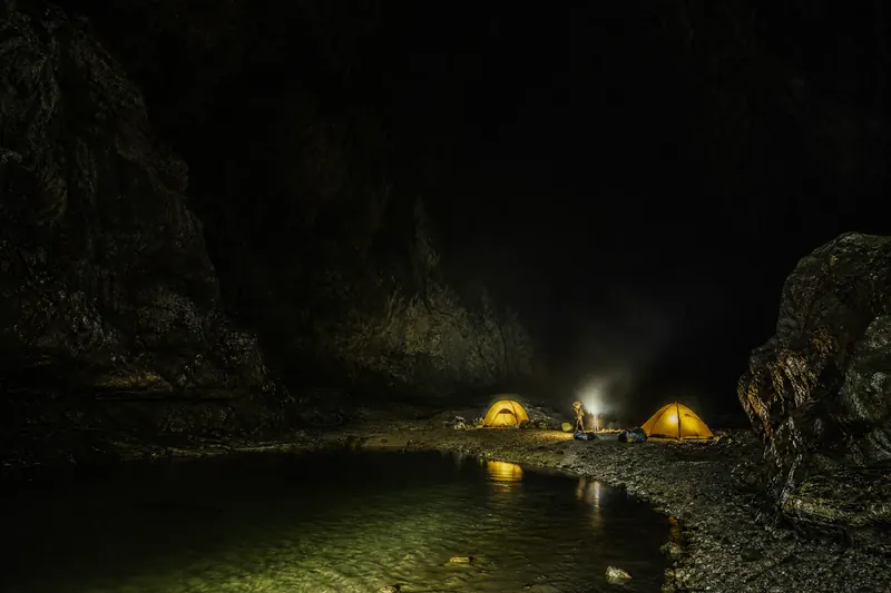 探险队在巨大黑暗洞穴大厅中搭建的地下营地，帐篷与头​灯点点亮光